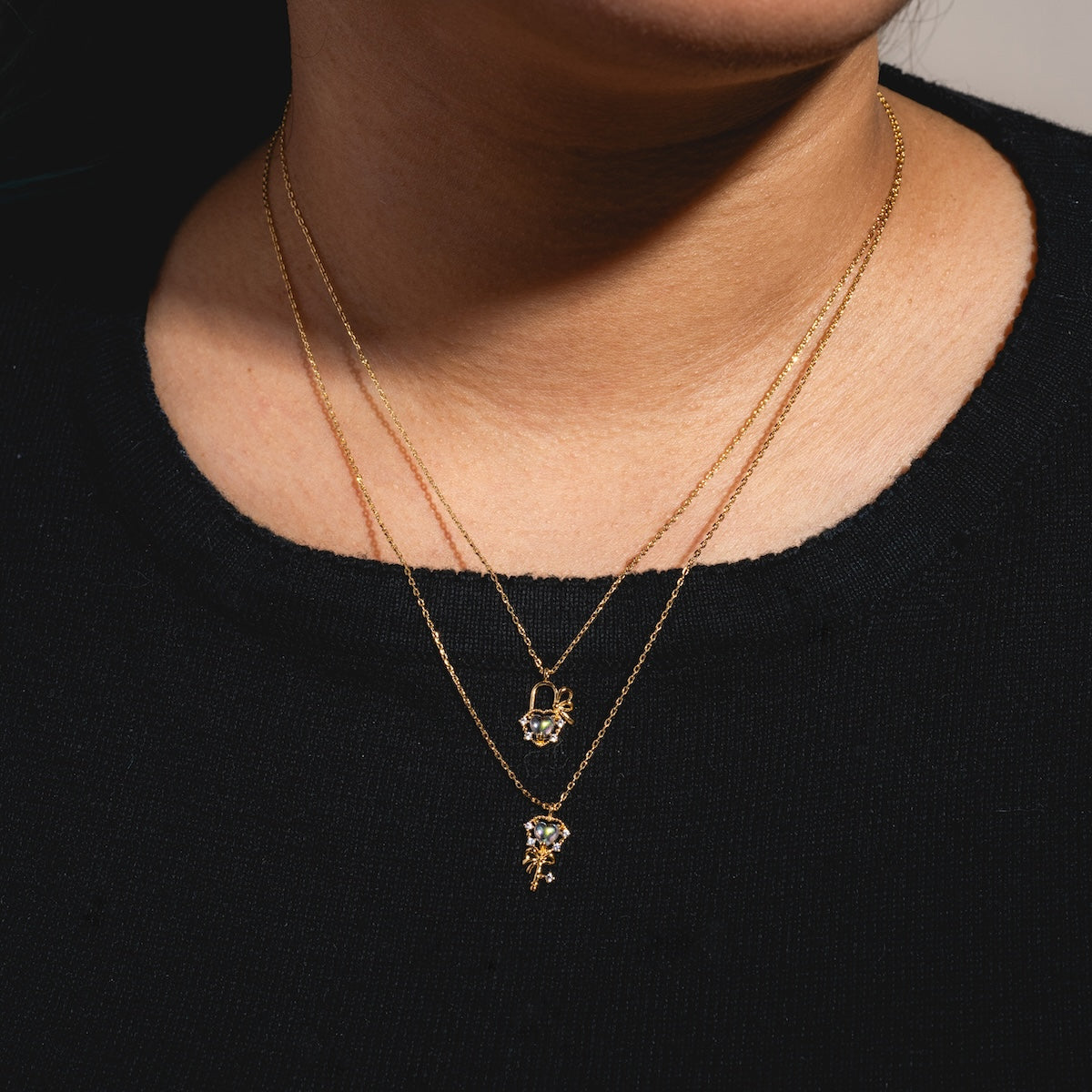 A close-up of a person wearing the Forever and Always Necklace Set Sample—two layered 18k yellow gold plated chains, each with unique pendants adorned with gemstone and CZ crystal details.