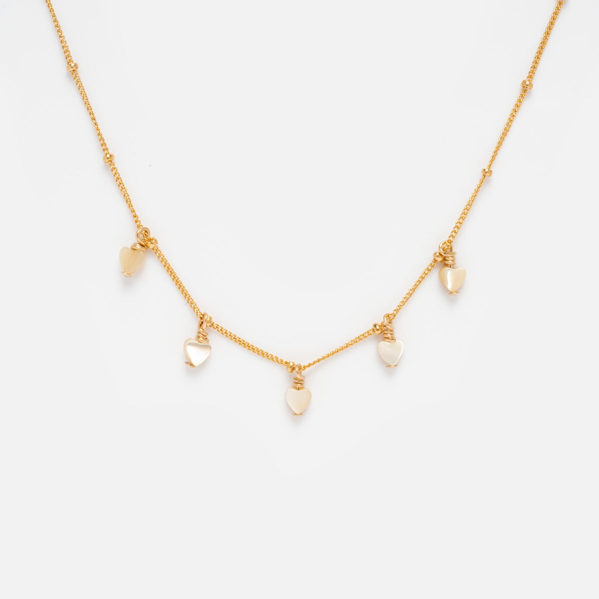 The Heart Bead Choker Sample is a delicate gold-filled necklace with five evenly spaced heart-shaped charms, some featuring shimmering mother of pearl, displayed on a plain white background.