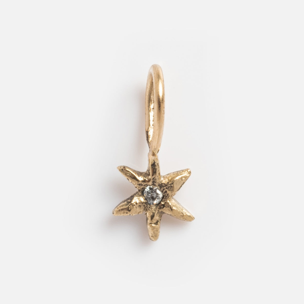 Acanthus 14k Solid Gold Tiny Charms: A small, star-shaped pendant with a textured finish and clear center gemstone, crafted from 14k yellow gold and attached to a circular loop, shown on a plain white background.