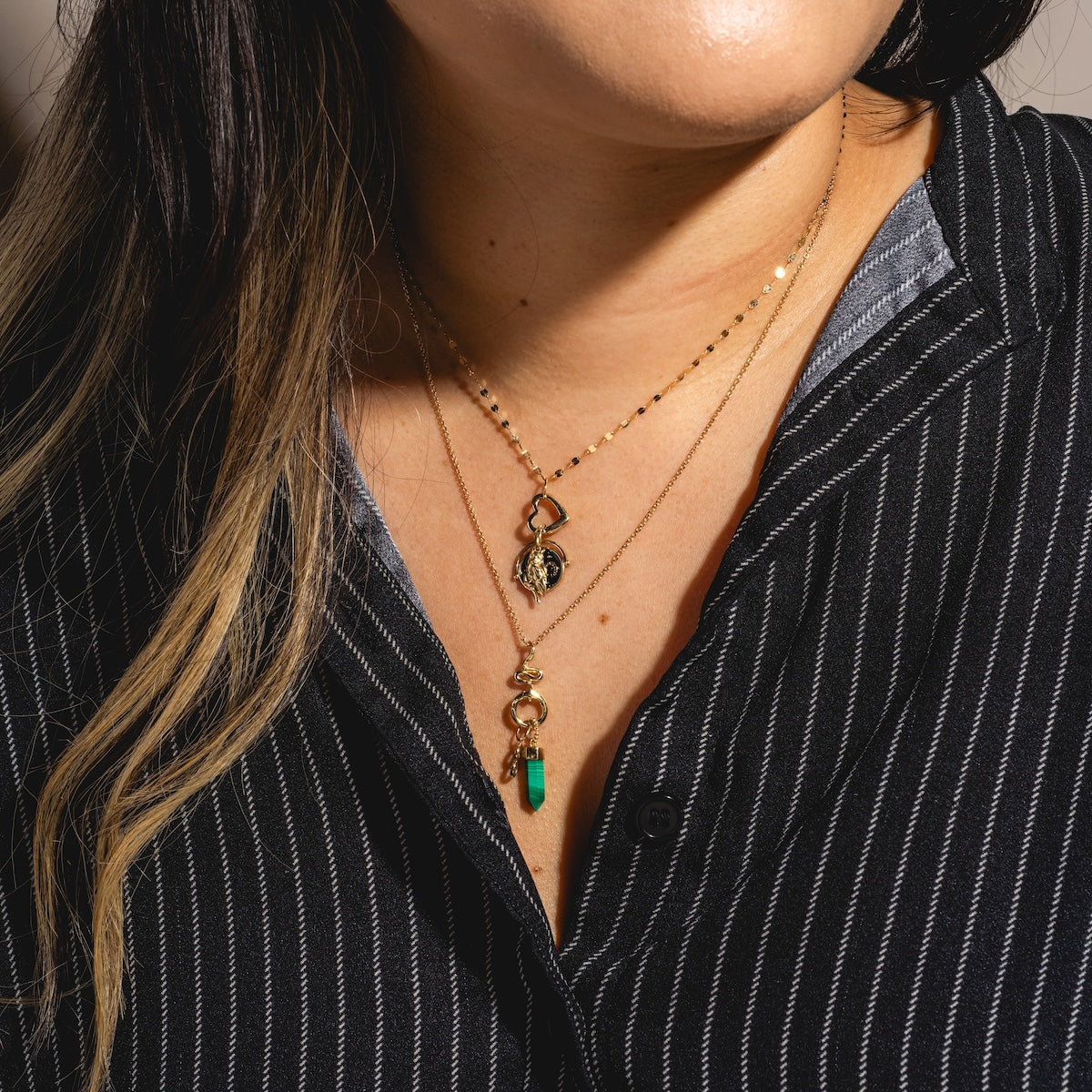 A woman wears a black pinstripe shirt and two layered gold necklaces—one featuring a personalized pendant and another, the Solid Gold Charm Clip, adorned with a turquoise stone.