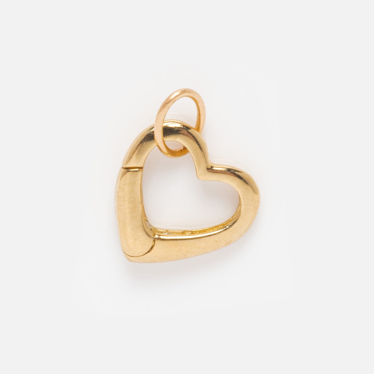 The Solid Gold Charm Clip is a heart-shaped pendant with a small top loop, ideal for attaching to bracelets or creating a custom necklace. Displayed on a plain white background.