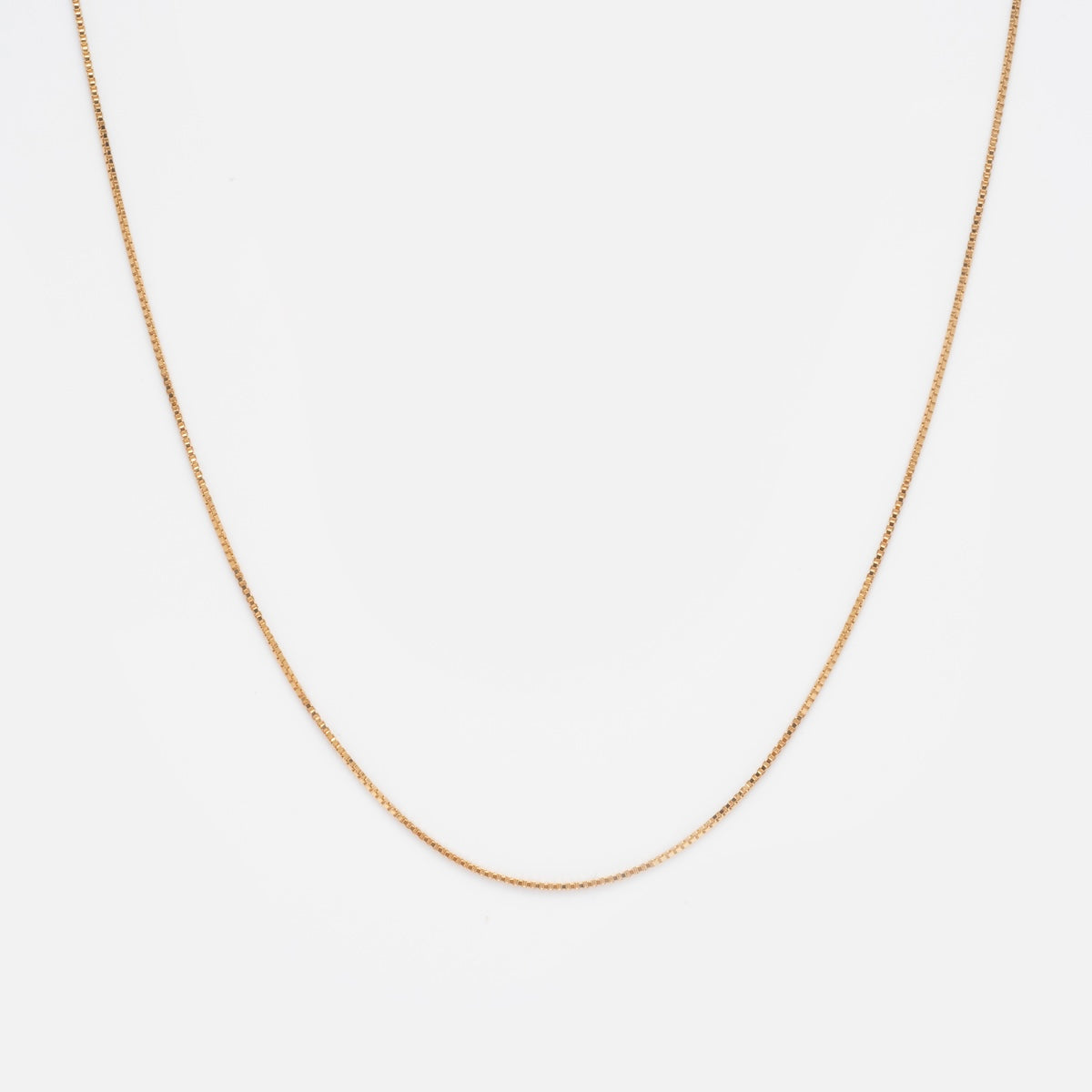 The Solid Gold Box Chain is a delicate, slinky necklace crafted from 9k solid gold, shown on a plain white background and elegantly curved.