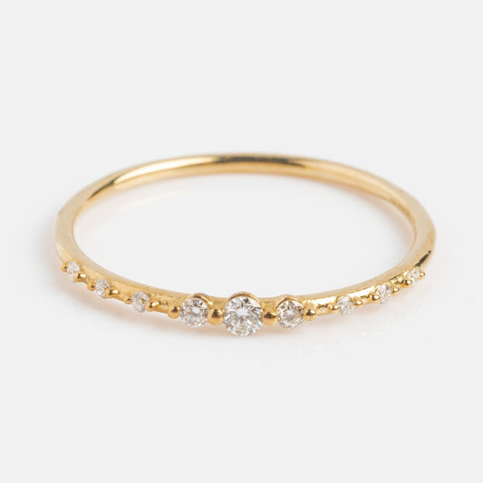 The Solid Gold Lab Diamond Sparkle Stacking Band features a row of round white lab diamonds, with the largest at the center and smaller ones tapering on each side, elegantly showcased against a white background.