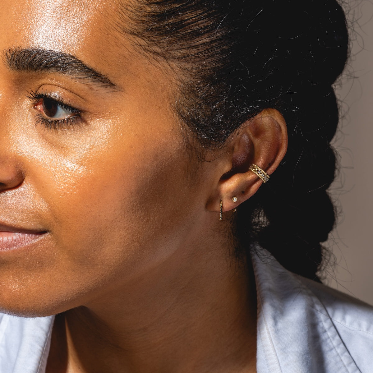 Close-up of a woman with braided hair wearing Solid Gold Pearl Ear Huggers on her left ear, perfect for everyday wear. She has smooth skin and is dressed in a light blue shirt.