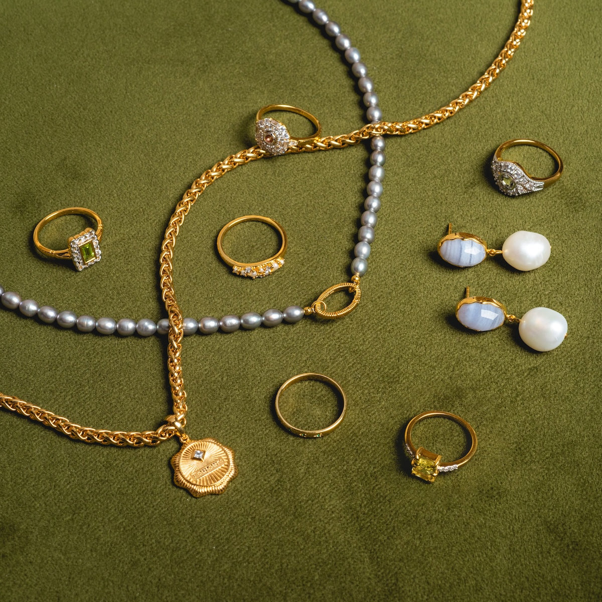The Madeline Pearl and Diamond Scatter Ring is displayed alongside earrings with pearls and blue stones, a 14k gold vermeil chain necklace, and a pearl necklace on a green velvet surface.