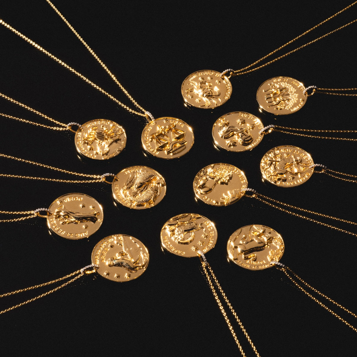 Twelve Vintage Inspired Zodiac Coin Necklaces, each with a unique zodiac symbol on a round gold pendant and matching chain, are arranged in a circle on a black background.