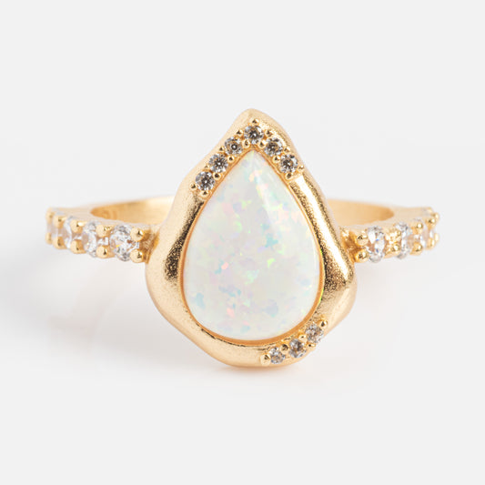 The Luster Solitaire Ring is a 14k gold plated opal ring with a pear-shaped center stone, clear gemstones surrounding it, and extra stones along the band, shown on a white background.