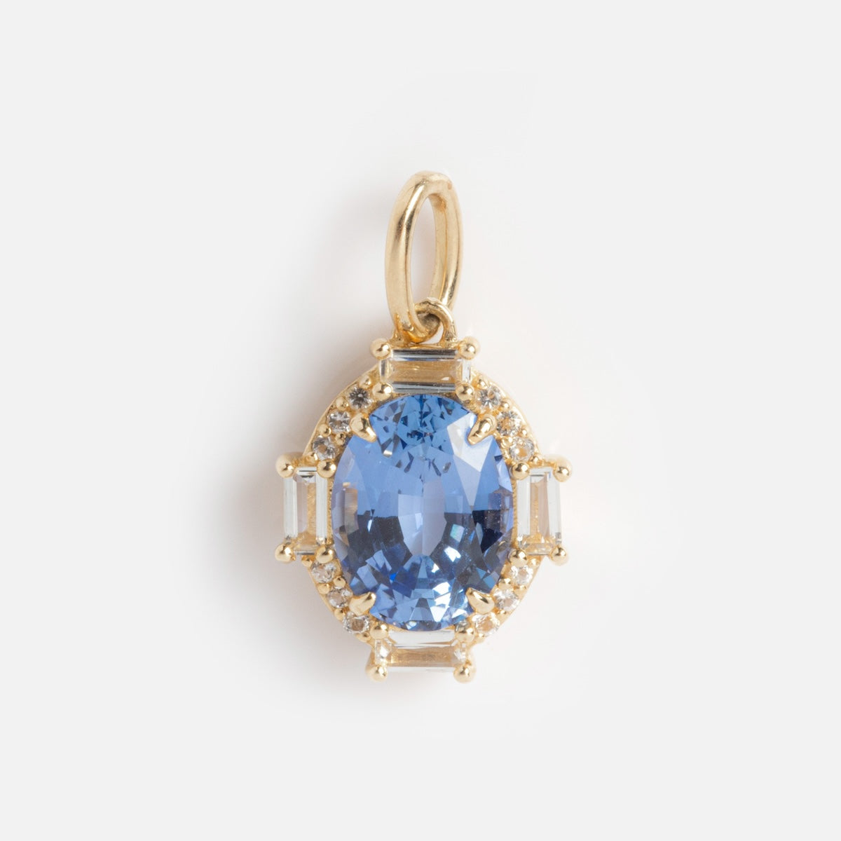 The Solid Gold Vintage Inspired Birthstone Charm features an oval-cut blue gemstone centerpiece, framed by small clear stones and rectangular accents, all set in solid gold and displayed against a plain white background.