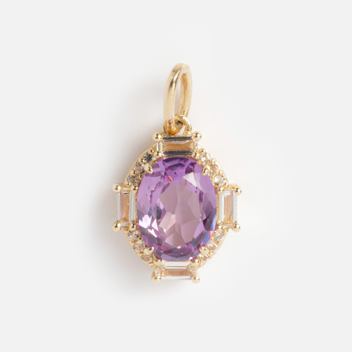 The Solid Gold Vintage Inspired Birthstone Charm features an oval-cut purple gemstone at the center, accented by small clear stones and gold detailing, with a gold loop for attaching to a chain. Shown against a white background.