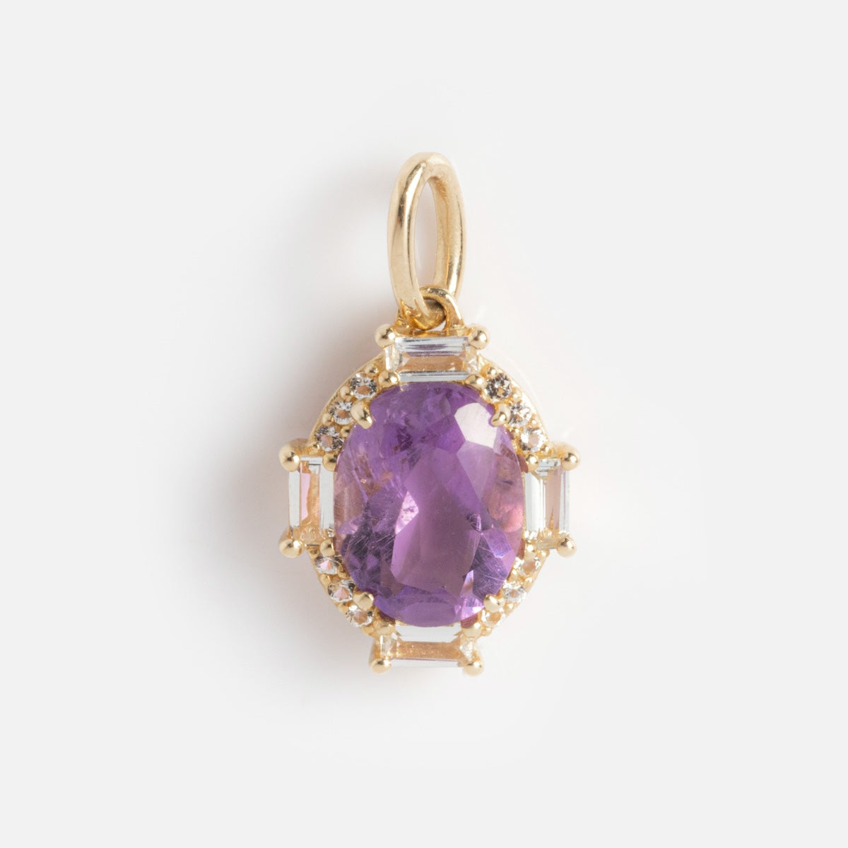 The Solid Gold Vintage Inspired Birthstone Charm features an oval purple gemstone surrounded by small clear stones and secured with prongs, displayed on a plain white background.