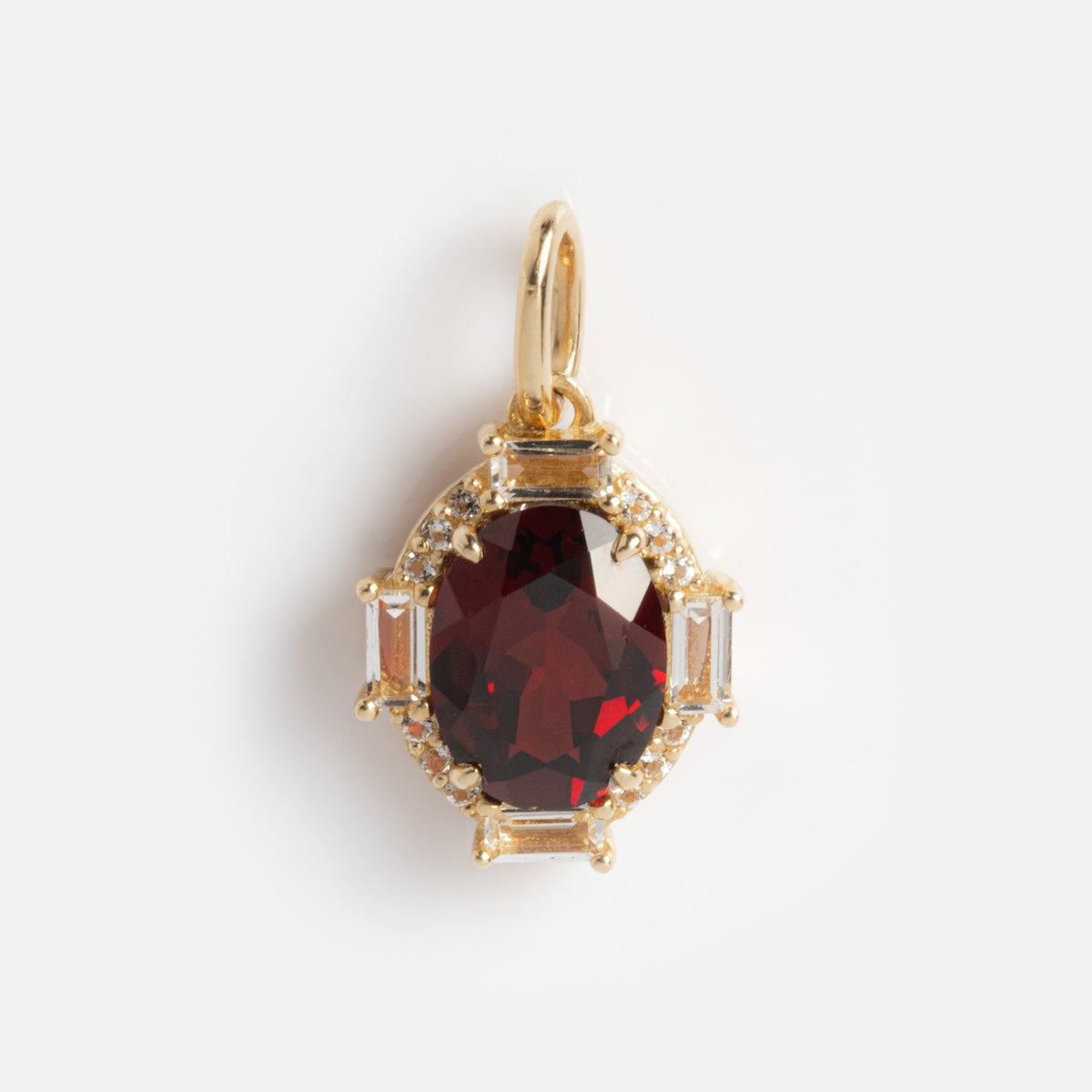 The Solid Gold Vintage Inspired Birthstone Charm showcases an oval deep red gemstone at the center, encircled by small clear stones and rectangular accents, all set in solid gold on a plain white background.