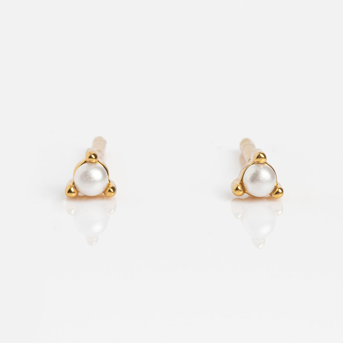 The Fabulous Studs are small stud earrings with round white pearls set in 14k gold plated triangular settings, shown on a white background.