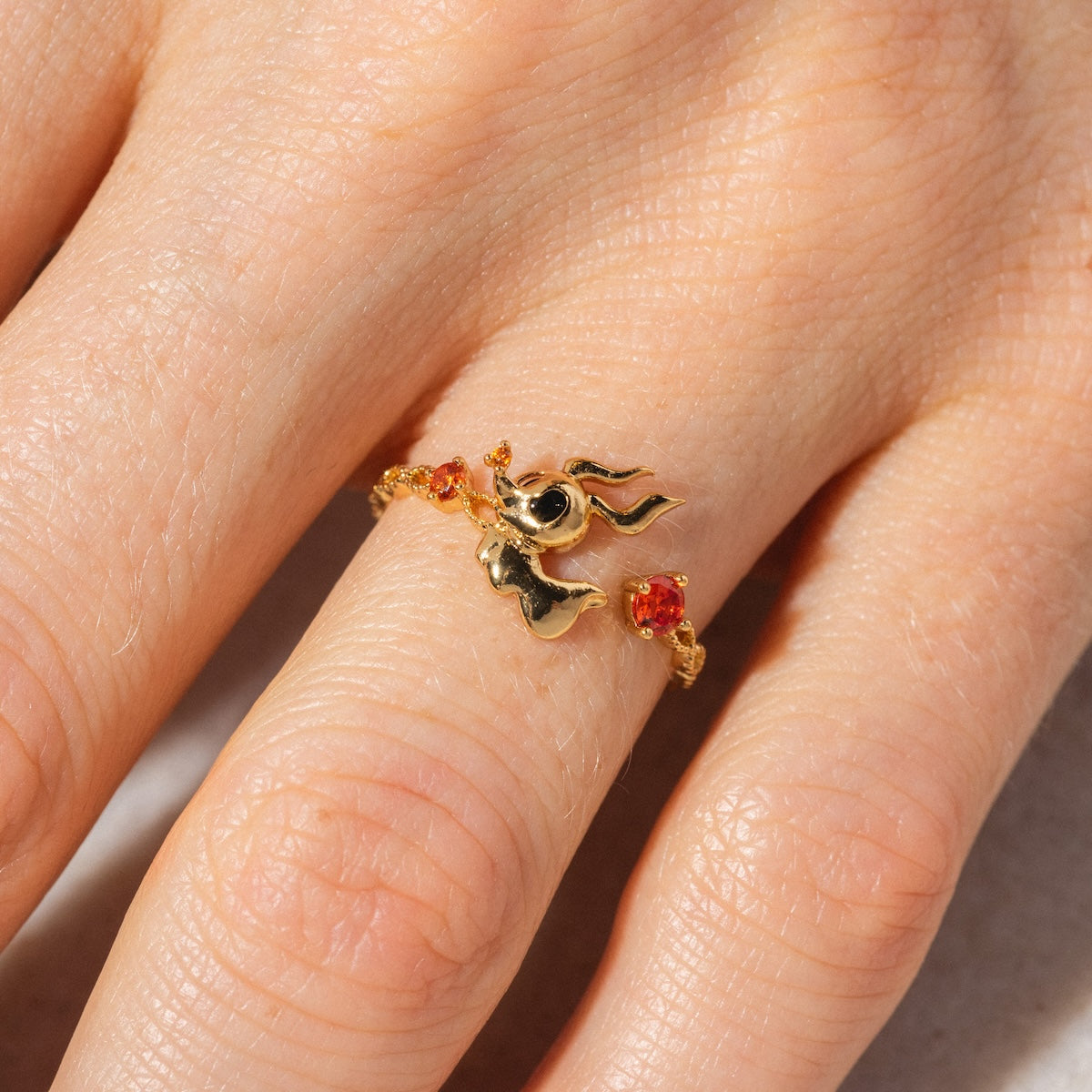 A close-up of a hand wearing the Disney Zero Adjustable Ring Sample Size 6.5, featuring a flame-shaped design with two small orange gemstones and plated in radiant 18k yellow gold.
