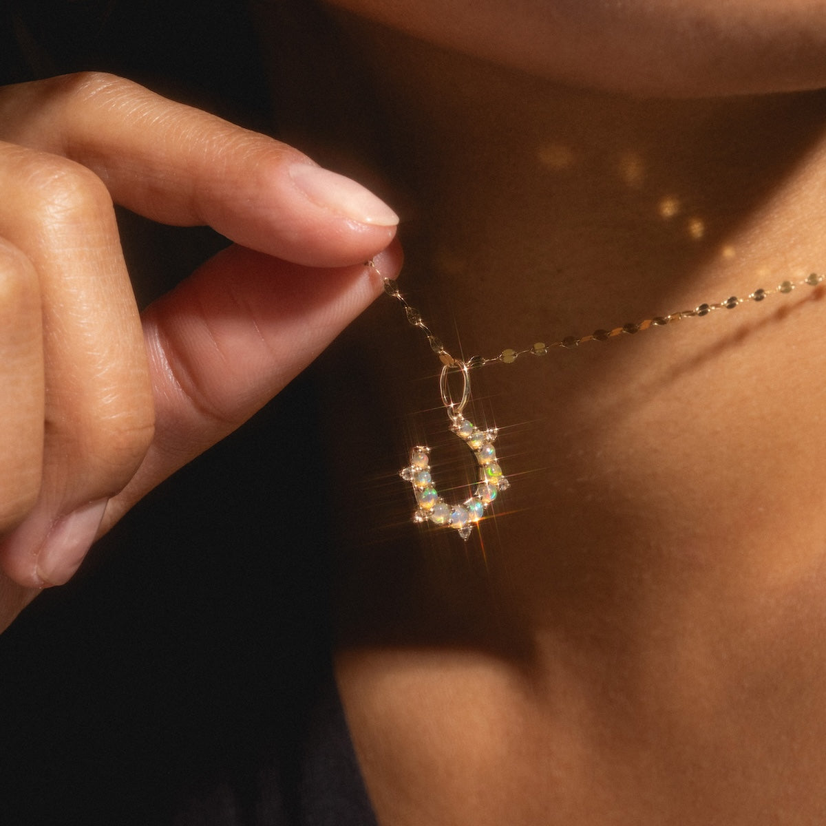 A person holds the Solid Gold Amulet Charm, a sparkling horseshoe-shaped pendant necklace, close to their neck—its shine and detail highlighted as a Local Eclectic exclusive.