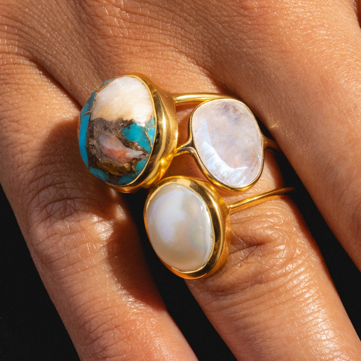 A bold, handcrafted Simple Semi Precious Pearl Ring with a large oval pearl adorns light brown skin, its beautiful gemstone setting radiating elegance.