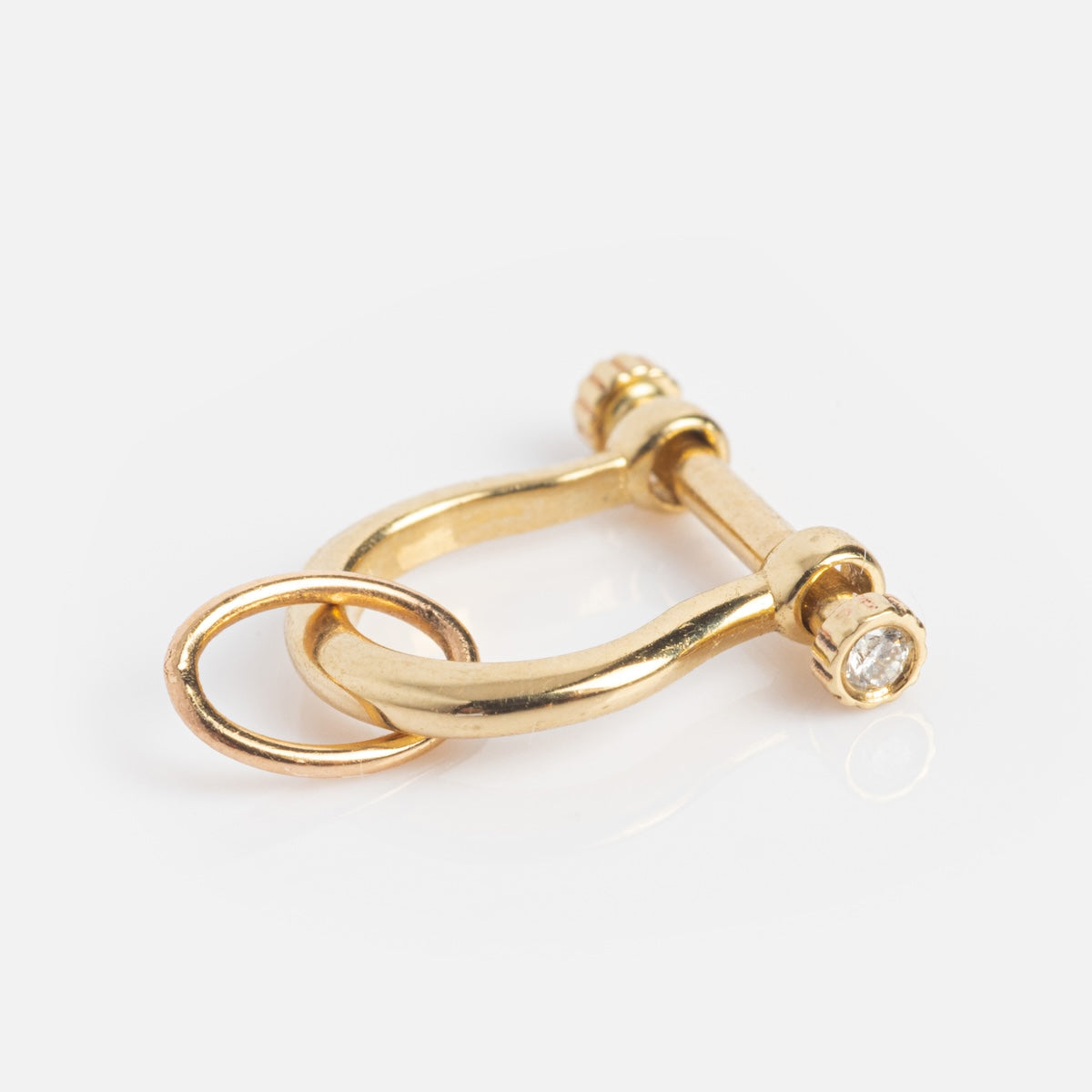 The Solid Gold Charm Clip is a small, rounded gold shackle with a screw pin and attached circular ring, ideal for adding charms to your necklace or bracelet. Shown on a plain white background.