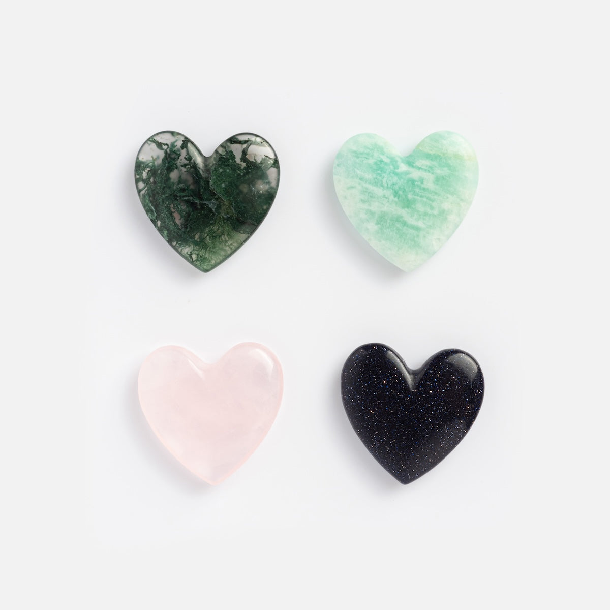 Four polished, heart-shaped stones—a perfect fit for the Solid Gold Changeable Crystal Locket Charm for Manifestation—are arranged in a 2x2 grid on white, showcasing dark green with white veining, light green, pale pink, and sparkling dark blue crystals.