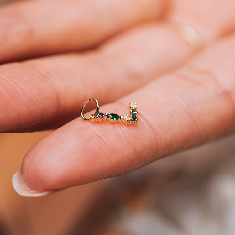The Solid Gold Gemstone Letter Charm, featuring colorful gemstones, is delicately balanced on a fingertip to showcase its fine details and expert craftsmanship.