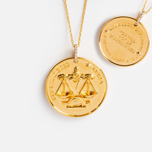 The Vintage Inspired Zodiac Coin Necklace features two gold vermeil chains. The front pendant displays the Libra zodiac sign, scales, and Sept 24 - Oct 23 LIBRA, while the back is engraved with a message and a lucky number.