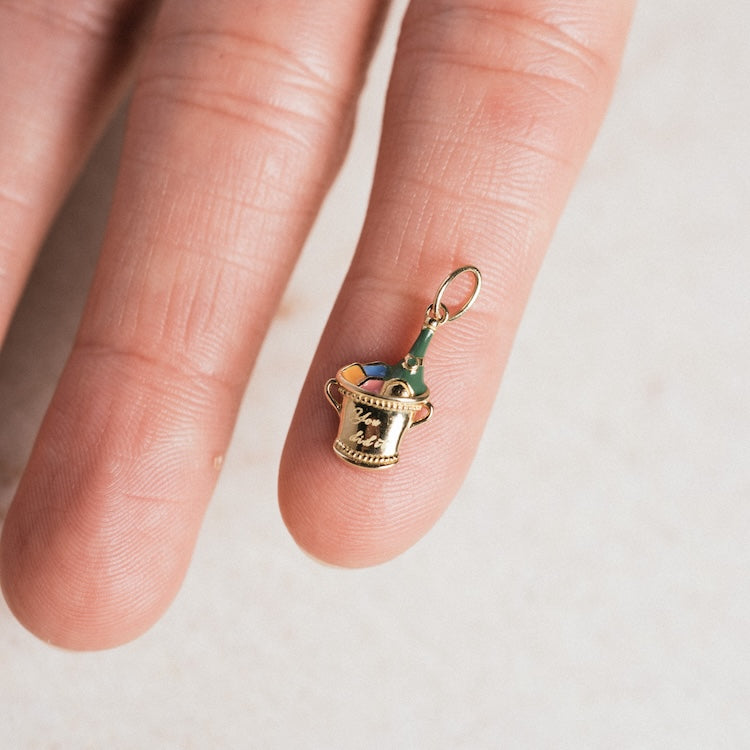 The Solid Gold Celebration Charm is a tiny 9k yellow gold charm shaped like an ice bucket with a green bottle, perfectly sized to rest on your fingertip—a unique piece for celebrating special moments.