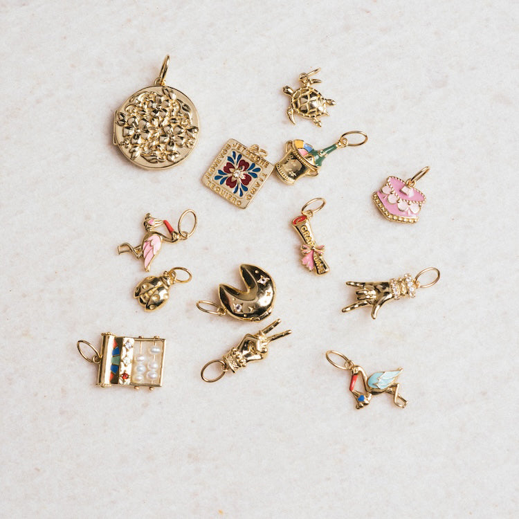 The Solid Gold Body Language Charm, part of a collection featuring animal, fortune cookie, flower, turtle, book, and pink cake charms, is displayed on a light textured surface for a decorative look.