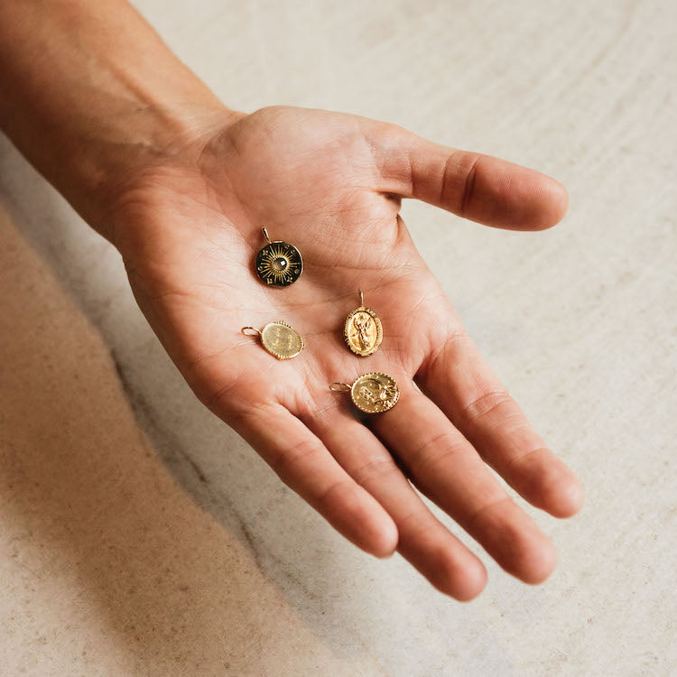 A hand holds four Solid Gold Coin Charms, each engraved with unique designs, on a light surface—an elegant showcase of Local Eclectics exclusive personalized jewelry.