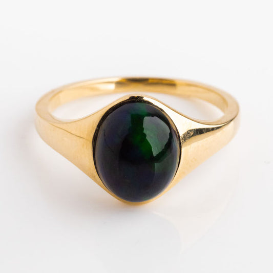 The Solid Gold Black Opal Aura Signet Ring showcases a smooth, oval dark green-black opal set at the center, photographed on a white background.