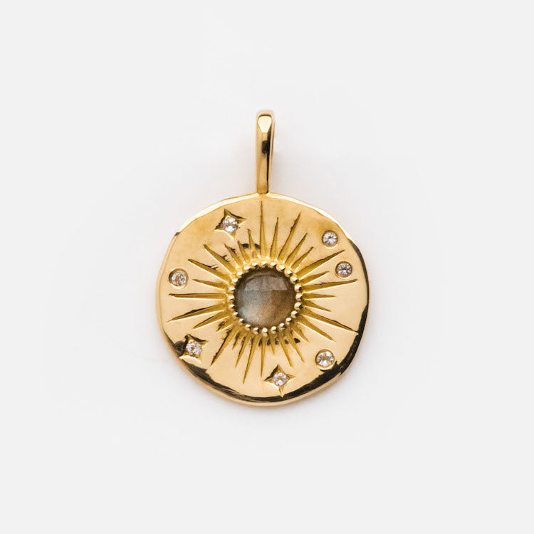 Exclusive to Local Eclectic, the Solid Gold Coin Charm features a round solid gold design with a textured sunburst pattern, a central translucent stone, and six small diamond-like stones surrounding the center.