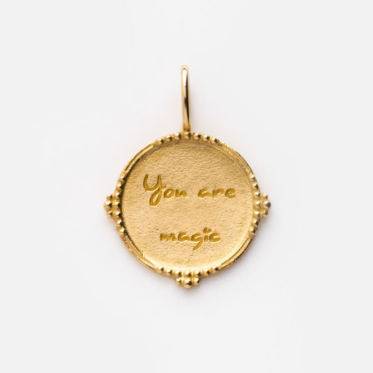 The Solid Gold Coin Charm is a round pendant with a textured edge and decorative beading, engraved with You are magic in cursive—a Local Eclectic exclusive shown against a plain white background.