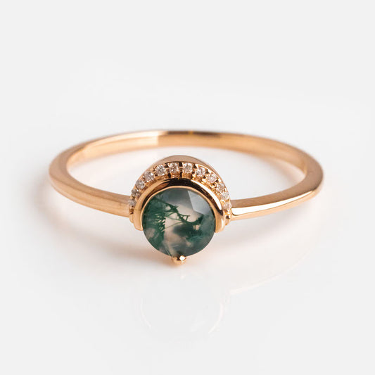 The 9kt Rose Gold Diamond and Moss Agate Celestial Sky Ring showcases a round green moss agate with natural inclusions, accented by sparkling diamonds along the band, all set against a plain white background.