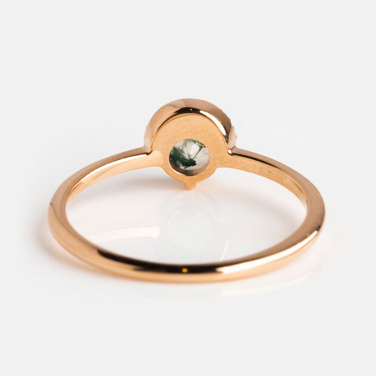 The 9kt Rose Gold Diamond and Moss Agate Celestial Sky Ring features a round green moss agate in a bezel setting with an open gallery beneath, elegantly displayed on a white surface.