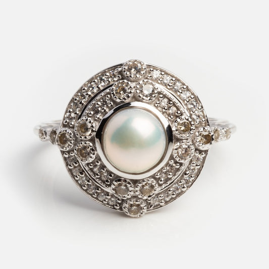 The Celestial Pearl Vintage Ring features a stunning central pearl surrounded by dual diamond halos, set on a delicate sterling silver band with sparkling diamonds.