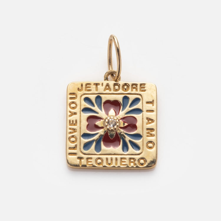 The Solid Gold Statement Charm is a square 9k yellow gold pendant with blue and red floral enamel, a small diamond accent, and “I LOVE YOU, JE T’ADORE, TI AMO, TE QUIERO” inscribed around the edges.