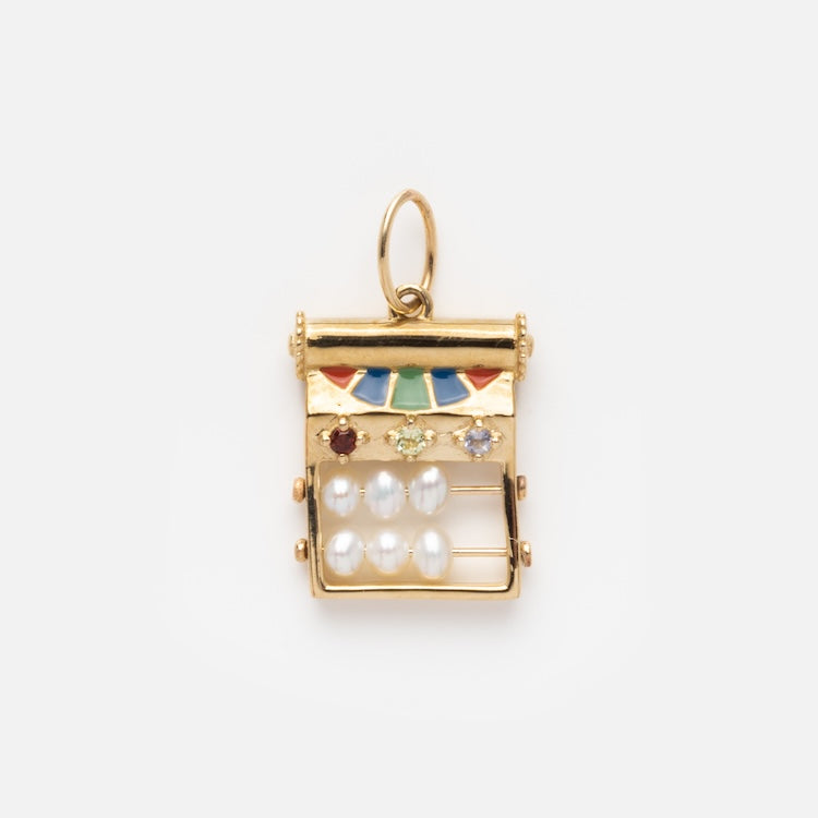 The Solid Gold Statement Charm is a 9k yellow gold geometric pendant with colorful enamel, small gemstones, six white pearls in two rows, and blue topaz accents, featuring a loop for easy attachment to your favorite chain.