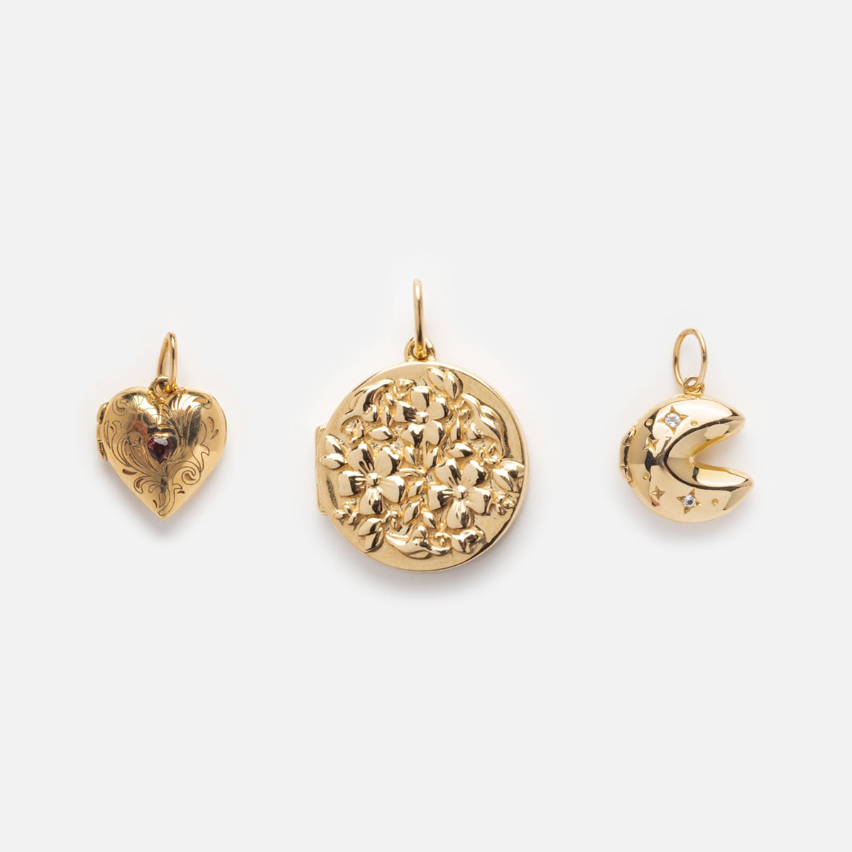 Three Solid Gold Locket Charms—a garnet heart locket, a floral etched locket, and a crescent moon with star details—are displayed side by side on a white background.