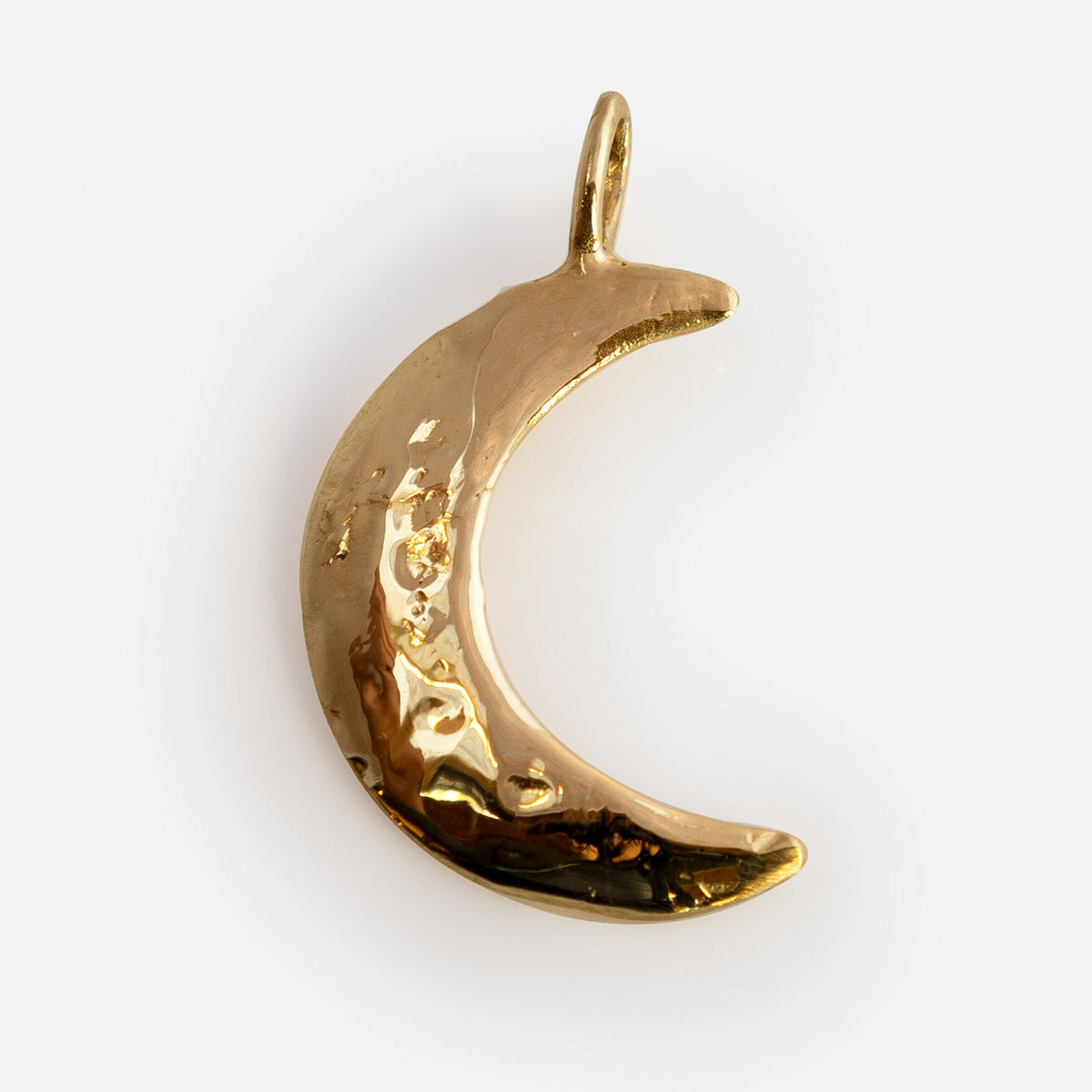 The Luiny x Local Eclectic Charms gold crescent moon pendant features a textured, slightly uneven surface, a small loop for attaching to a chain, and is crafted from solid brass charms. Shown against a white background.