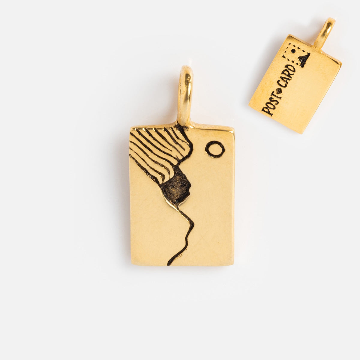 The Charms by Hunt of Hounds pendant features a gold vermeil rectangular charm with an abstract face and wavy hair on one side, and a postcard motif with POSTCARD text and stamp on the other. Ideal for layering with other charms.