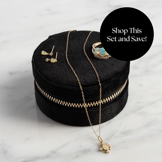 The Solid Gold 2025 October Capsule Opal Full Set, featuring earrings, a necklace, and a ring with opal accents, is displayed on a round black velvet zippered box atop marble. A black circle reads: Shop This Set and Save! Plus Free Gift.
