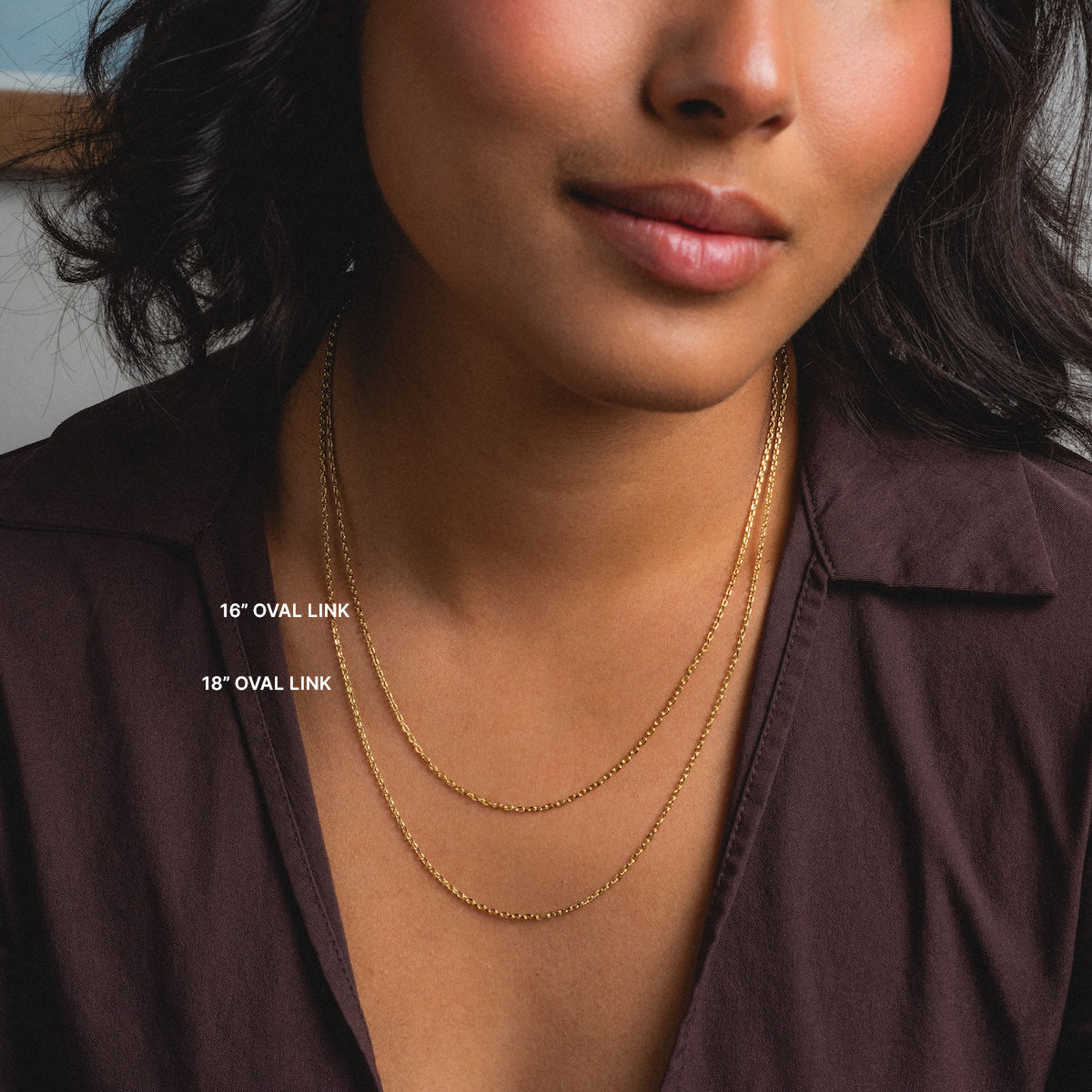 A woman in a dark brown top models two gold Chain For Charms paperclip necklaces, 16-inch and 18-inch, elegantly layered on her neck.