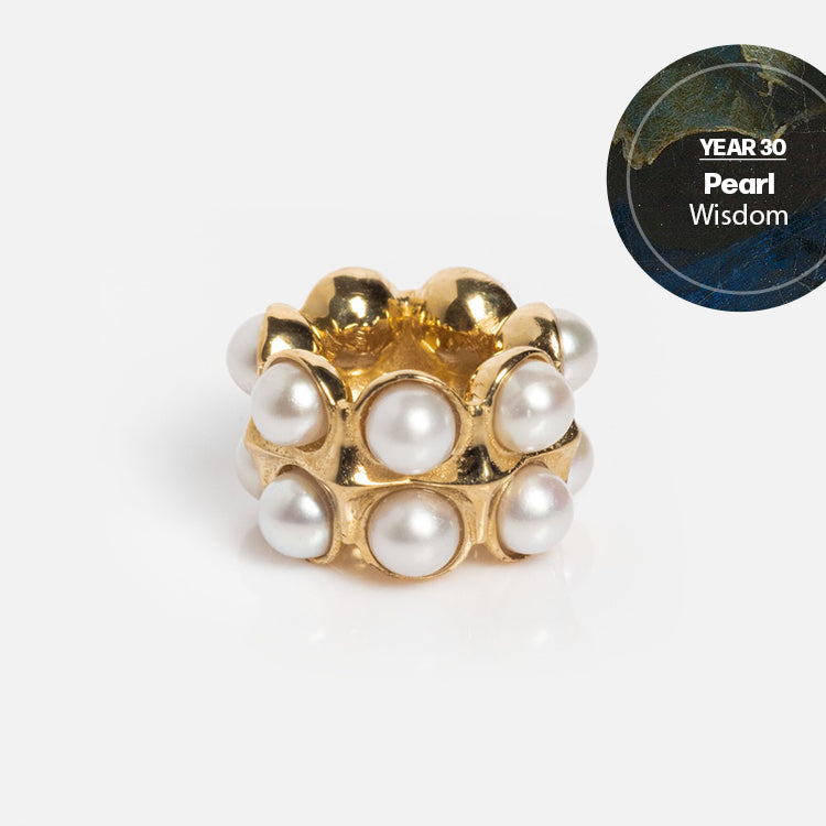 The Solid Gold Anniversaire Charm, featuring two stacked rows of round white pearls and a YEAR 30: Pearl - Wisdom label, makes a perfect milestone jewelry piece, set against a dark marble background.