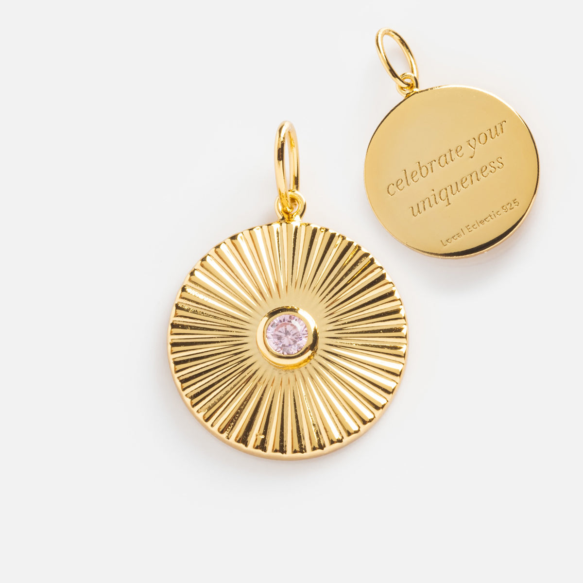 Two round 14k gold plated pendants: one with a pink gemstone and radiating design, the other is the Mantra Empowerment Coin Charm engraved with celebrate your uniqueness and Leoni Elevevich 925—perfect mantra jewelry.