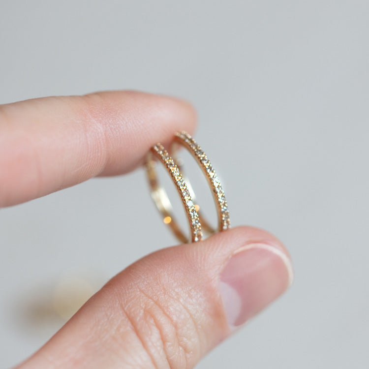 A hand holds two Solid Gold Diamond Hoops, crafted from thin 10k gold and encrusted with lab-created diamonds, shown against a plain light background.