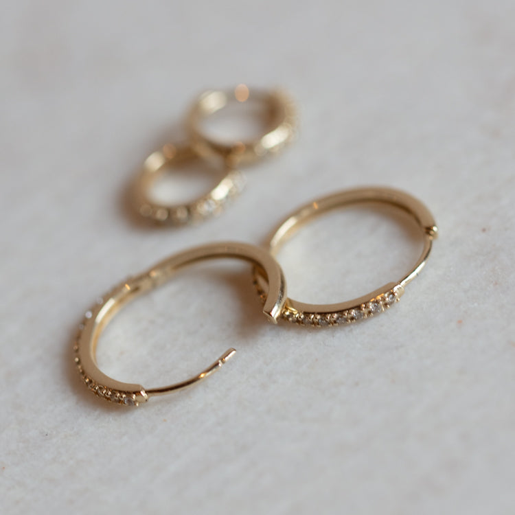 Two pairs of Solid Gold Diamond Hoops—one large, one small—each set with lab created diamonds, are displayed on a light, textured surface.