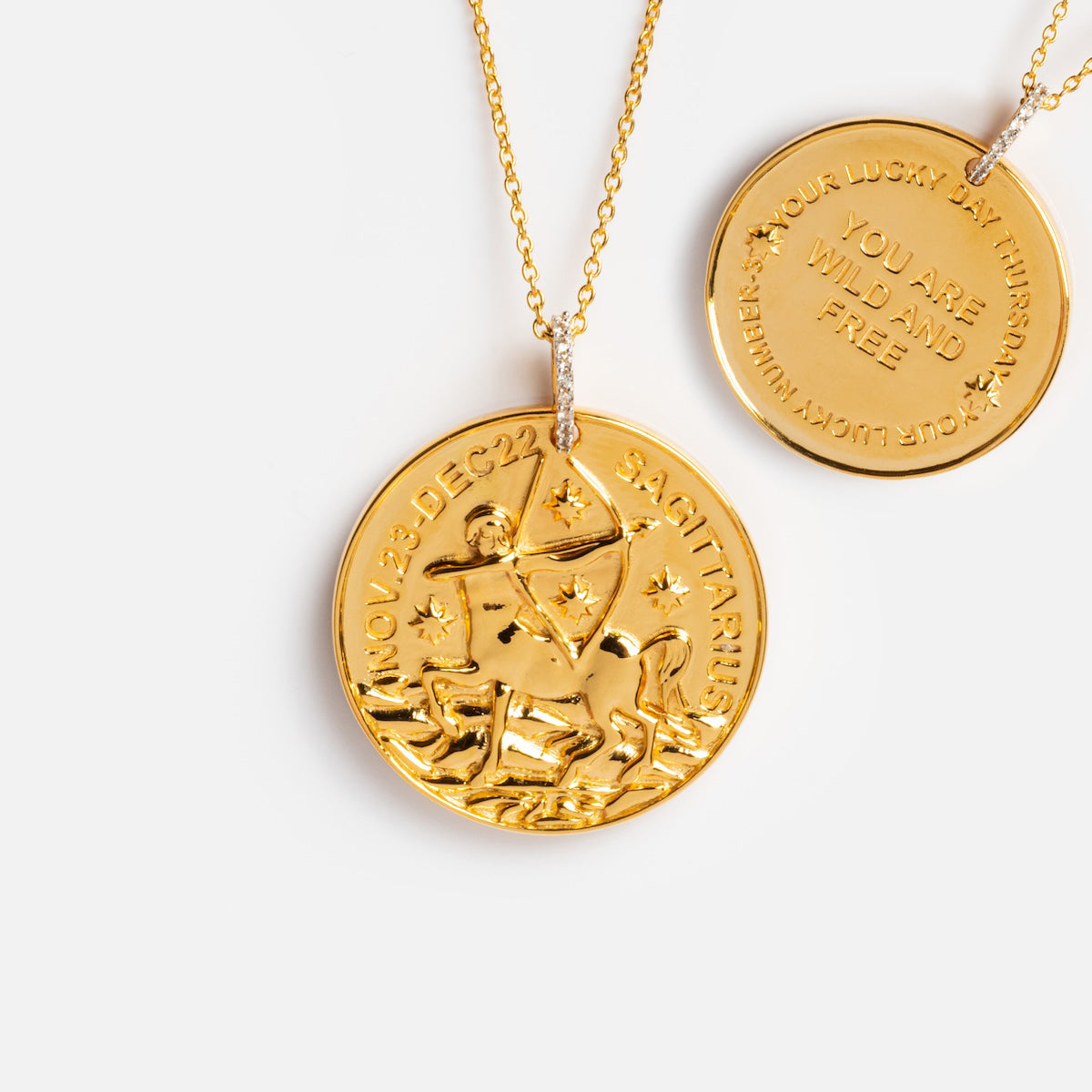 The Vintage Inspired Zodiac Coin Necklace showcases an engraved Sagittarius archer with stars and NOV 23-DEC 22 SAGITTARIUS, while a second pendant inscribed YOU ARE WILD AND FREE is partially visible in the background.