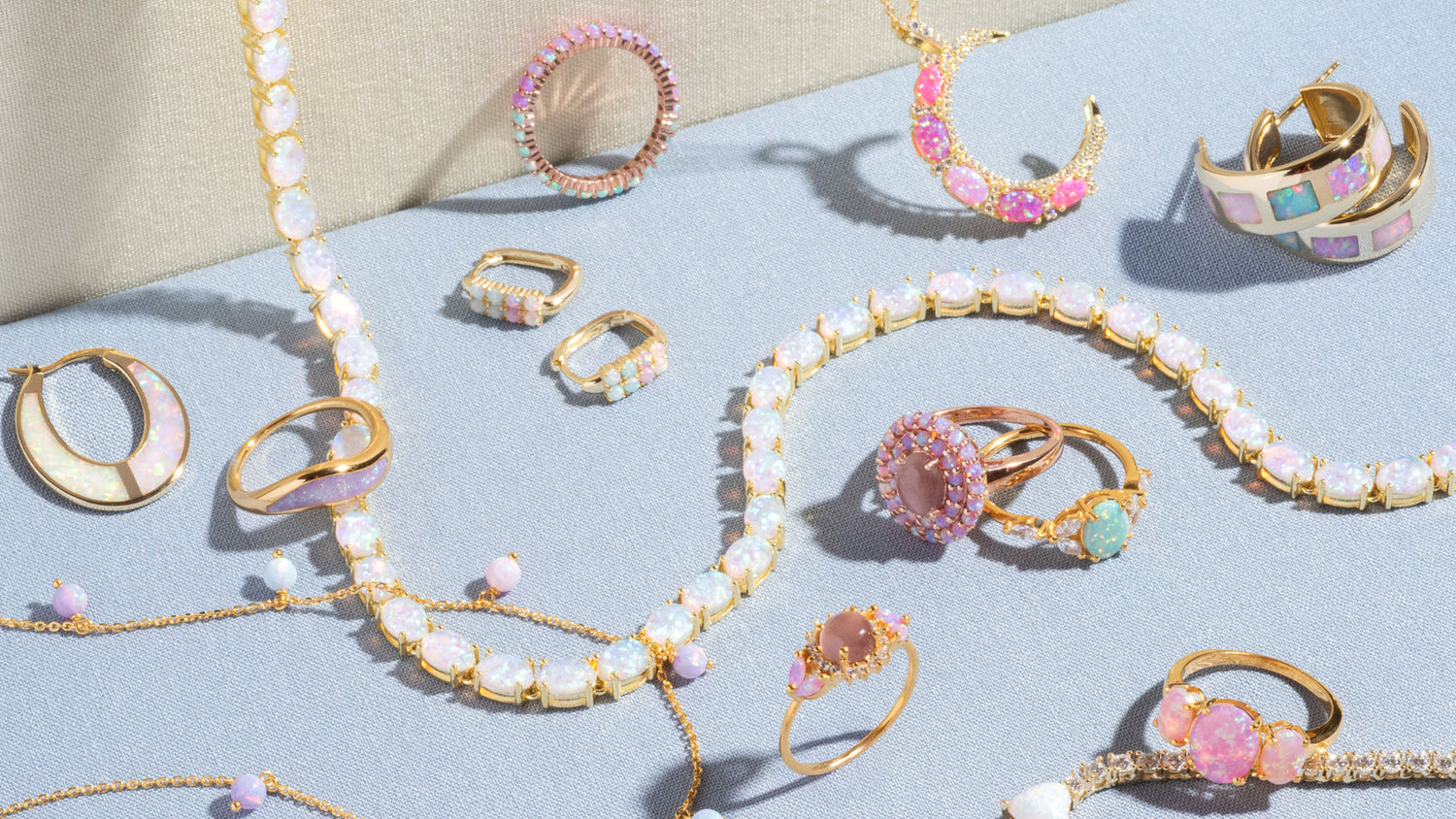 Several pieces of gold jewelry with pastel opals laying on a light blue fabric