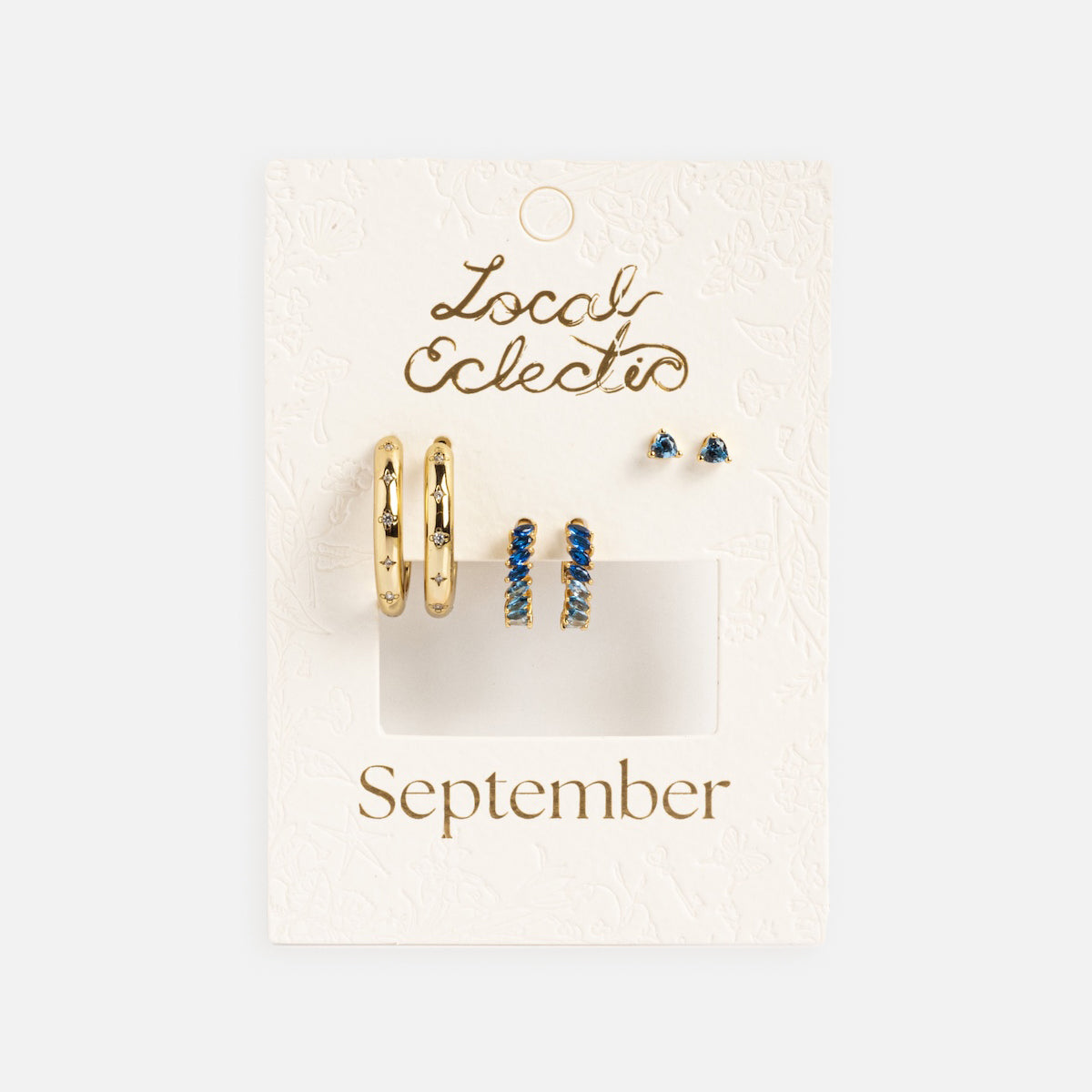 The Bold Birthstone Earring Set includes gold-plated hoops, blue stone huggies, and blue studs, ideal for a custom ear stack. Presented on a white "Local Eclectic" card labeled "September.