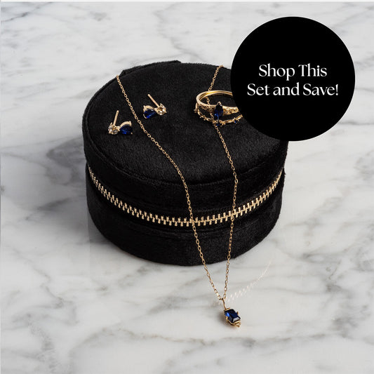The Solid Gold 2025 September Capsule Blue Sapphire Full Set with Free Gift features a necklace, earrings, and rings with deep blue stones from the Family Gold collection, displayed on a black velvet box atop white marble. Shop This Set and Save!.