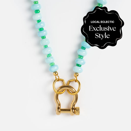 The Gemstone Carabiner Necklace features alternating light blue and green beads with a gold clasp. A black badge in the top right reads “Local Eclectic Exclusive Style.”.