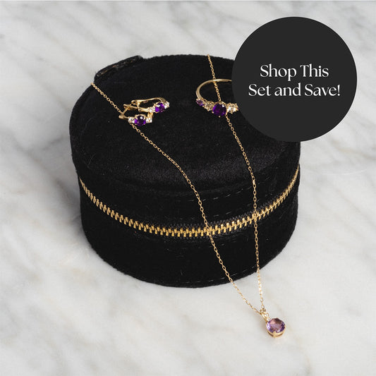 Discover the Solid Gold 2025 February Capsule Amethyst Statement Set—includes a free gift! Featuring earrings, a ring, and necklace with amethyst stones, elegantly displayed in a round black velvet box on marble. “Shop This Set and Save!”.