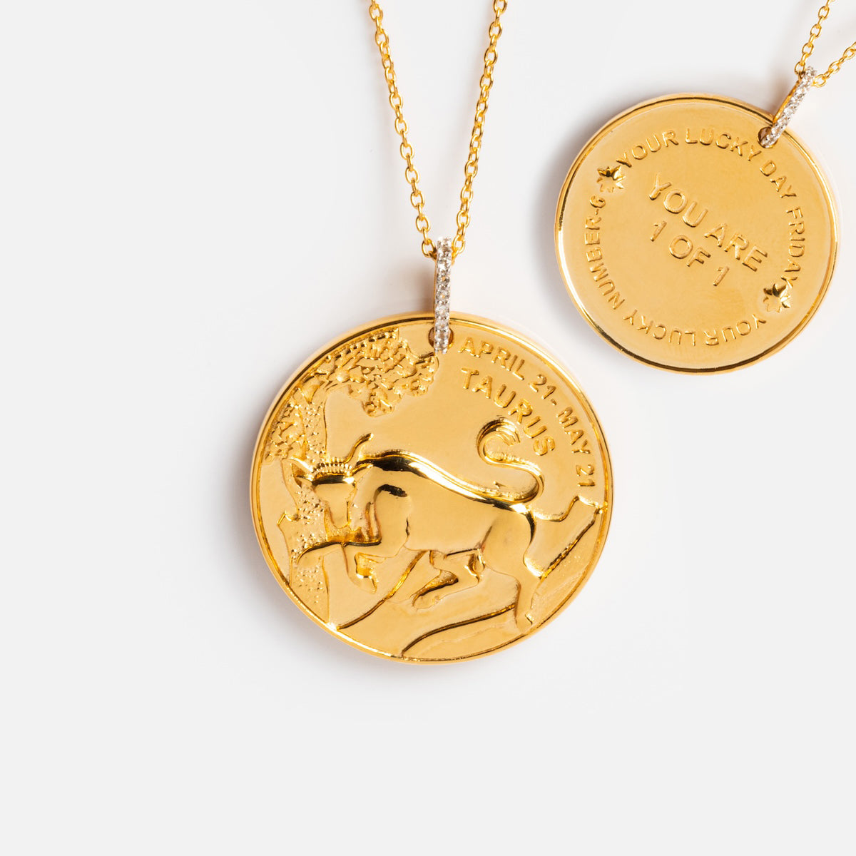 Two gold vermeil necklaces: a vintage charm with raised bull and TAURUS details, and the Vintage Inspired Zodiac Coin Necklace inscribed YOU ARE 1 OF 1, both featuring round pendants with delicate script.